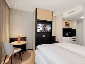 A hotel room with a bed, a desk with a chair, a TV mounted on the wall, a microwave, and a small kitchenette. - smartments Bielefeld Hauptbahnhof (Bielefeld)