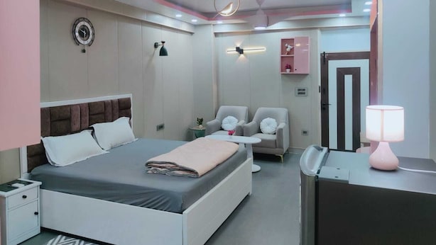 A modern bedroom with a bed, bedside tables, a desk, chairs, and a mirror. - Luxury Studio Apartment at Noida (Noida)
