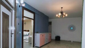 A hallway with a marble floor, a blue and pink cabinet, a chandelier, and a decorative wall piece. - Luxury Studio Apartment at Noida (Noida)