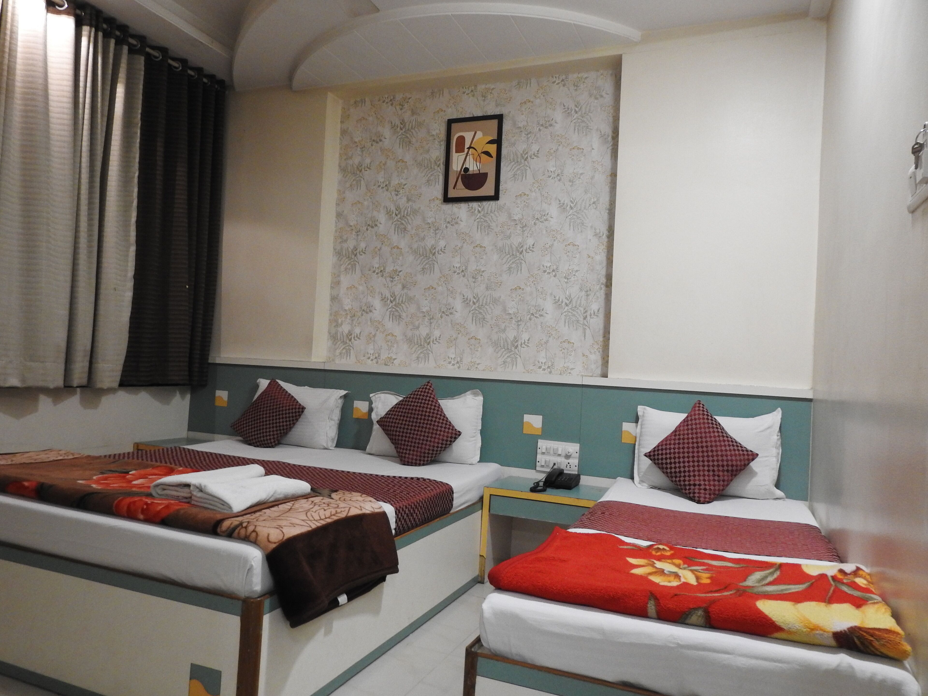 A hotel room with two beds, each with a different patterned bedspread. There is a small table with a phone and a power outlet.