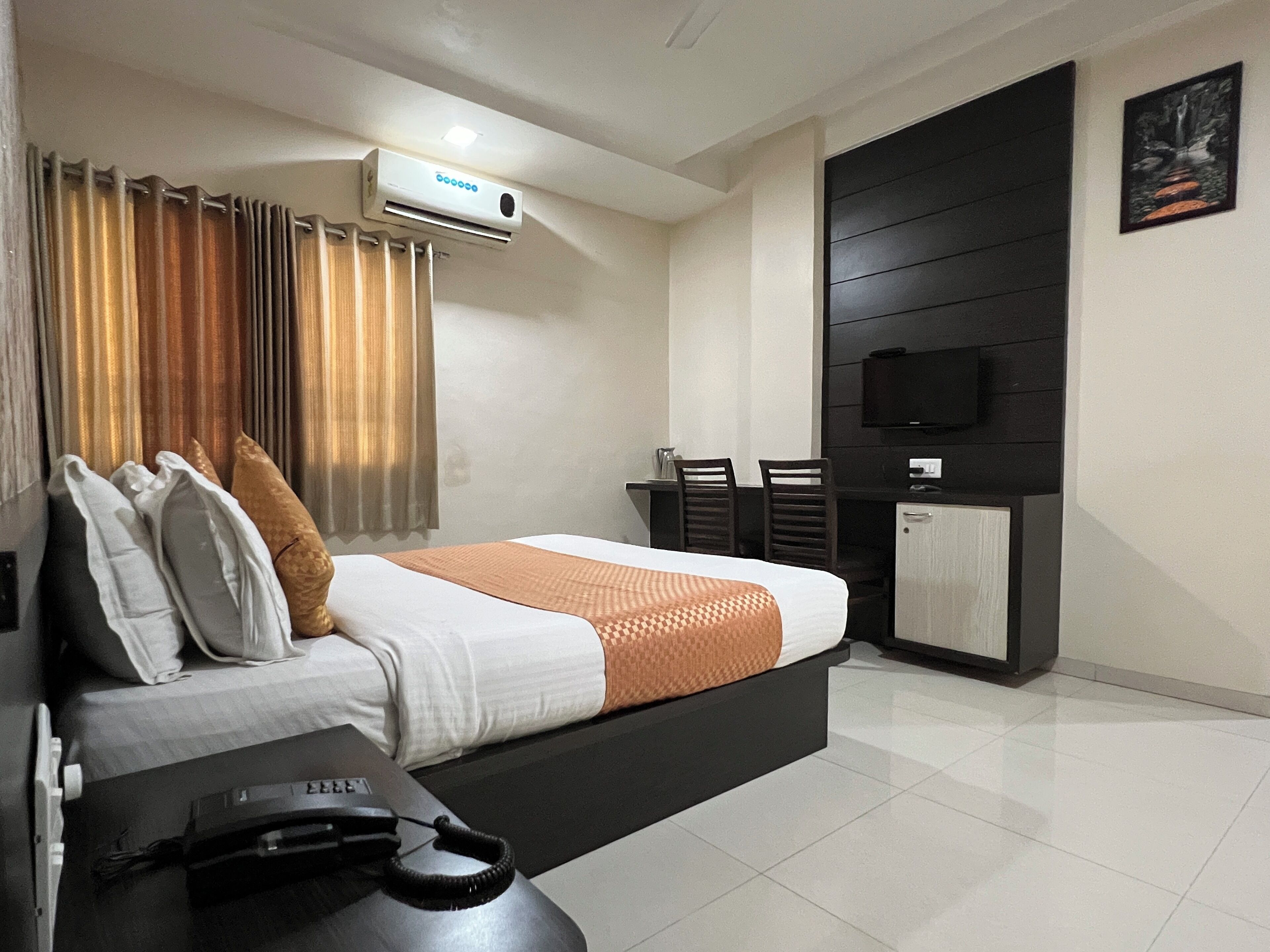 A modern hotel room with a bed, a desk, a chair, a television, and an air conditioning unit.