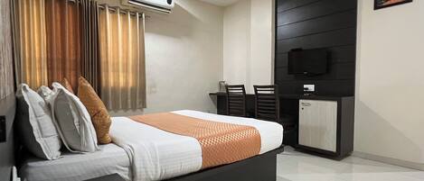 A modern hotel room with a bed, a desk, a chair, a television, and an air conditioning unit.