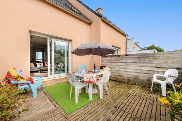 Une terrasse extérieure avec une table et des chaises, une terrasse en bois et une porte-fenêtre coulissante donnant sur un espace intérieur.