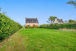 A house with a paved driveway, a well-maintained lawn, and a hedge on the left.