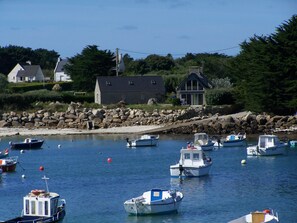 A harbor with multiple boats, a stone wall, and houses in the background.