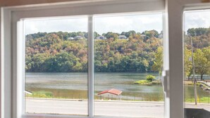 Vista desde una ventana de un lago con casas en una colina, una estructura de techo rojo pequeño y una carretera en primer plano.
