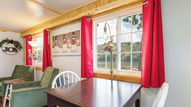 Una habitación acogedora con techo de madera, una mesa de comedor, dos sillones verdes, una silla blanca y una ventana con cortinas rojas.