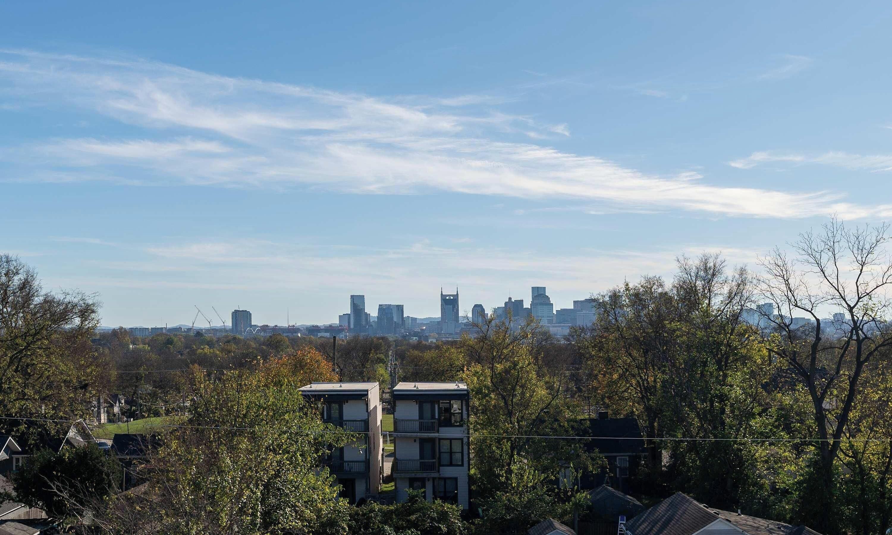 Un quartier résidentiel avec des immeubles d’appartements modernes, entouré d’arbres et offrant une vue lointaine sur les gratte-ciel de la ville.