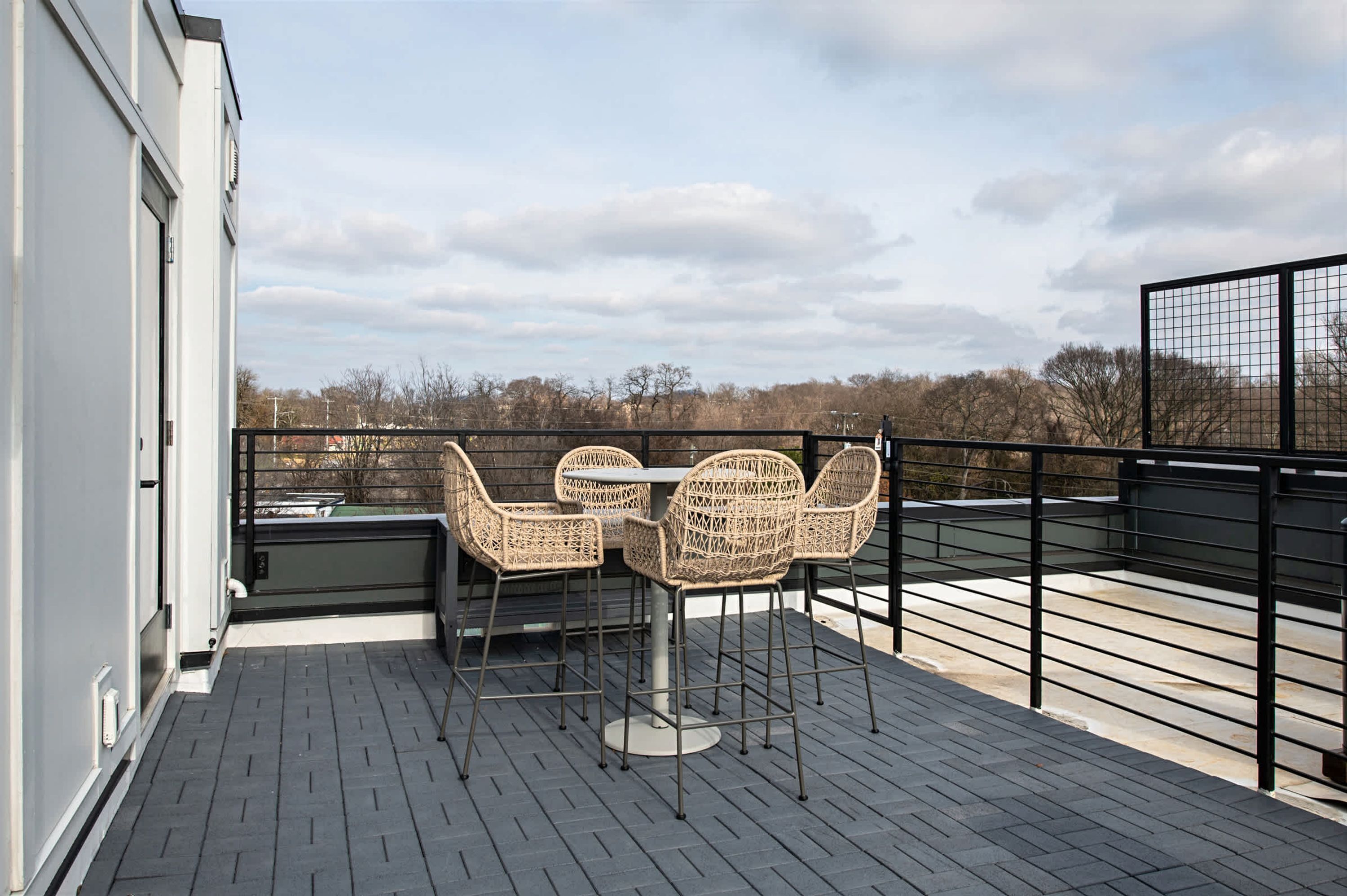 A rooftop terrace with wicker chairs and a table, overlooking a cityscape.