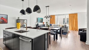 A modern kitchen with a central island, black pendant lights, and a dining area with a sofa and table. - Rooftop Hot Tub Skyline Views Near Broadway (Nashville)