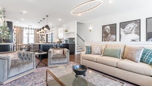 A modern living room with a sofa, armchairs, and a coffee table. There is a staircase leading to the upper floor. - Rooftop Fire Pit Skyline Views Near Broadway (Nashville)