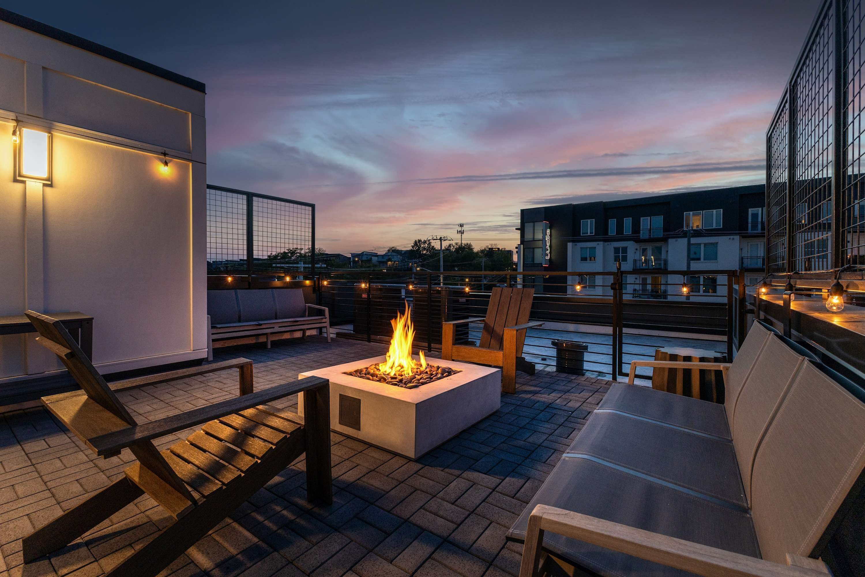 A rooftop terrace with a fire pit, seating, and a view of the cityscape at dusk.
