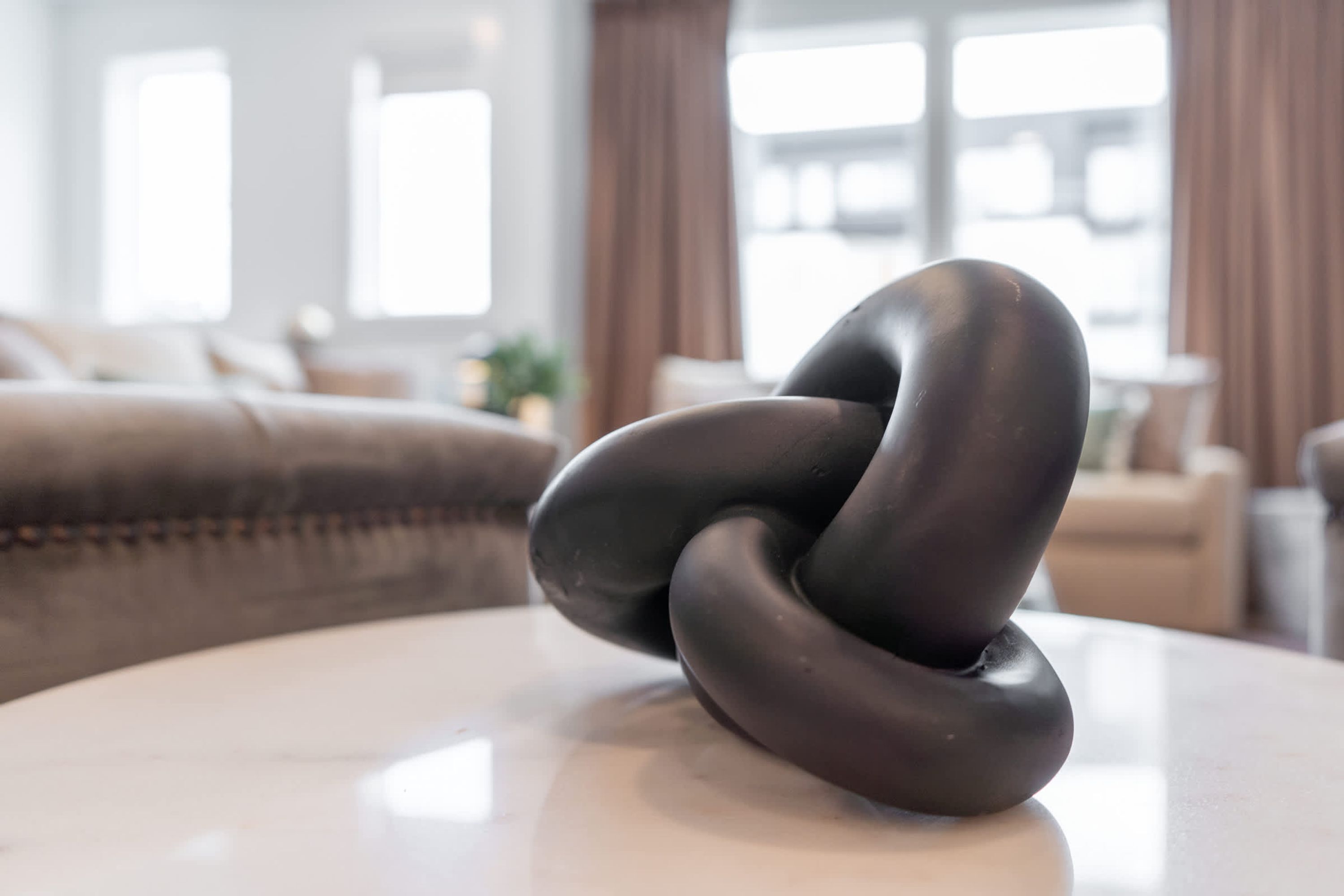 Una scultura scura e astratta su un tavolo bianco in un soggiorno moderno con un divano e tende.