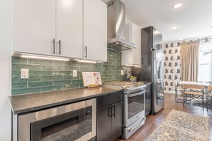 A modern kitchen with stainless steel appliances, green tiled backsplash, and a dining area with a table and chairs. - Rooftop Fire Pit Skyline Views Near Broadway (Nashville)