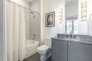 A modern bathroom with a bathtub, toilet, and vanity. - Rooftop Fire Pit Skyline Views Near Broadway (Nashville)