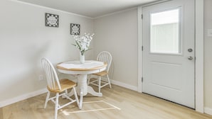A dining area with a round table, two white chairs, a vase with flowers, and two framed pictures on the wall.
