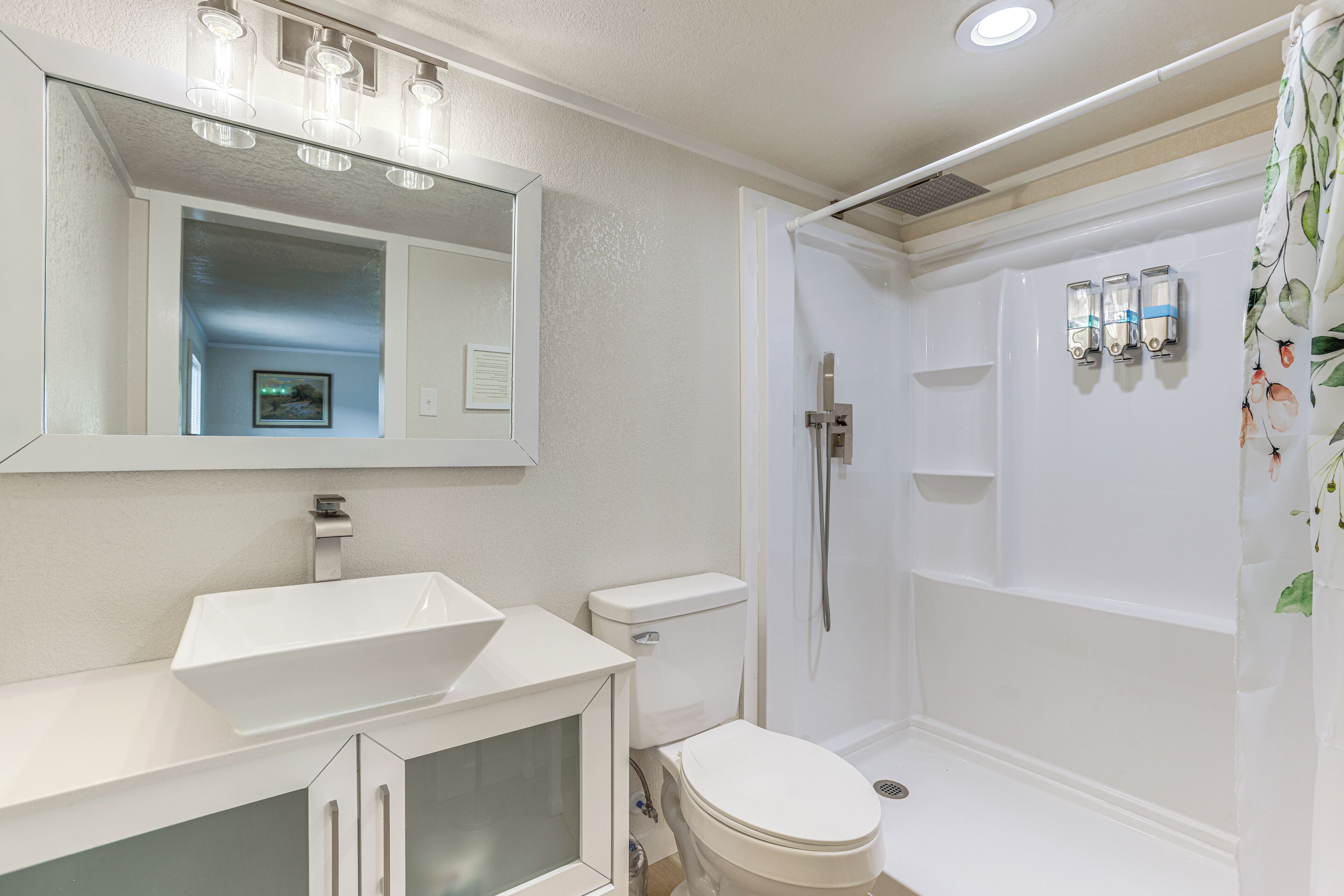A bathroom with a white sink, mirror, toilet, and shower.