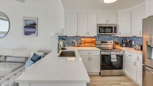 A modern kitchen with white cabinets, a central island, and a microwave. - Walk to Sand! Modern Okaloosa Island Condo (Fort Walton Beach)