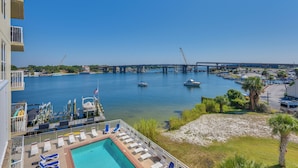 A pool area with lounge chairs, a view of the marina, and a bridge in the background. - Walk to Sand! Modern Okaloosa Island Condo (Fort Walton Beach)