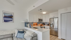 A modern kitchen with white cabinets, a stainless steel refrigerator, and a built-in island with a sink. - Walk to Sand! Modern Okaloosa Island Condo (Fort Walton Beach)