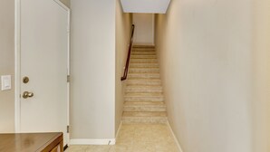 A hallway with a carpeted staircase, a white door, and a wooden bench. - Walk to Public Transit: Gated Oceanside Abode! (Oceanside)