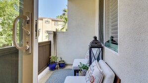 A balcony with a white sofa, two potted plants, a patterned rug, and a lantern. - Walk to Public Transit: Gated Oceanside Abode! (Oceanside)