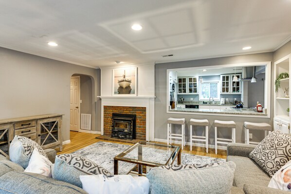 A living room with a fireplace, a kitchen with bar stools, and a dining area. - Large Yard w/ Pond: Family Retreat in New Albany! (New Albany)