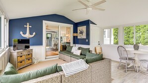 A living room with a blue accent wall, a television, wicker furniture, and a ceiling fan. - Coastal Charmer < 1 Mi to South Kingstown Beach (South Kingstown)
