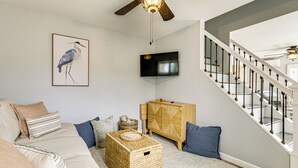 A living room with a sofa, a television, a ceiling fan, and a staircase. - Coastal Charmer < 1 Mi to South Kingstown Beach (South Kingstown)