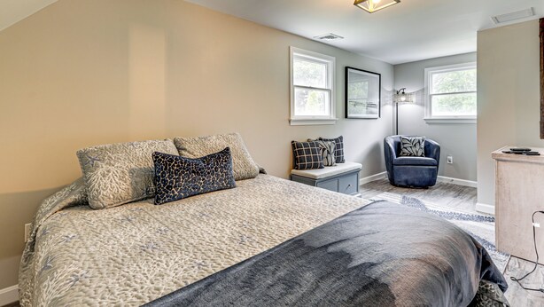 A bedroom with a large bed, a chair, a desk, and two windows. - Coastal Charmer < 1 Mi to South Kingstown Beach (South Kingstown)