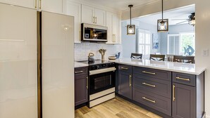 A modern kitchen with white cabinets, dark countertops, a stainless steel refrigerator, a microwave, and an oven. There are pendant lights above the counter. - Coastal Charmer < 1 Mi to South Kingstown Beach (South Kingstown)