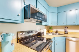 A kitchen with blue cabinets, a stainless steel stove, a coffee maker, and a blender.