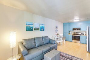 Ein modernes Wohnzimmer mit grauem Sofa, einem Esstisch mit Stühlen und einer Küche mit blauen Schränken und Edelstahlgeräten.