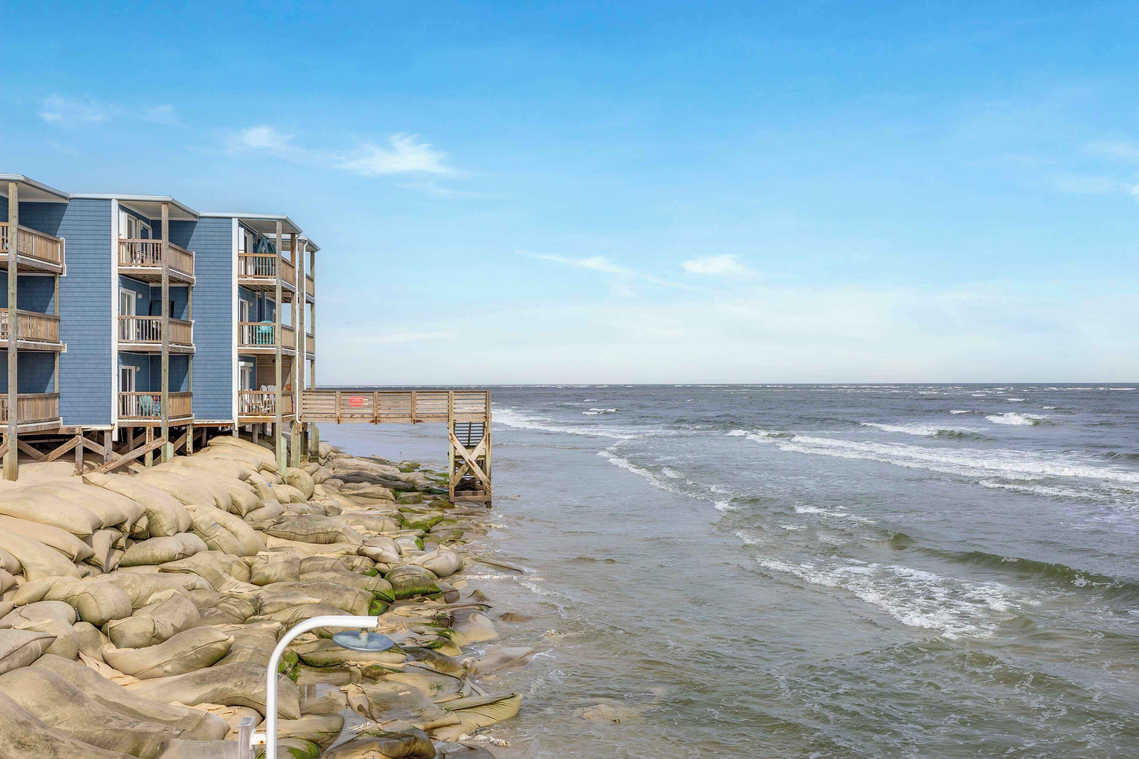 A beachfront building with multiple balconies and a wooden deck extending over the rocks.