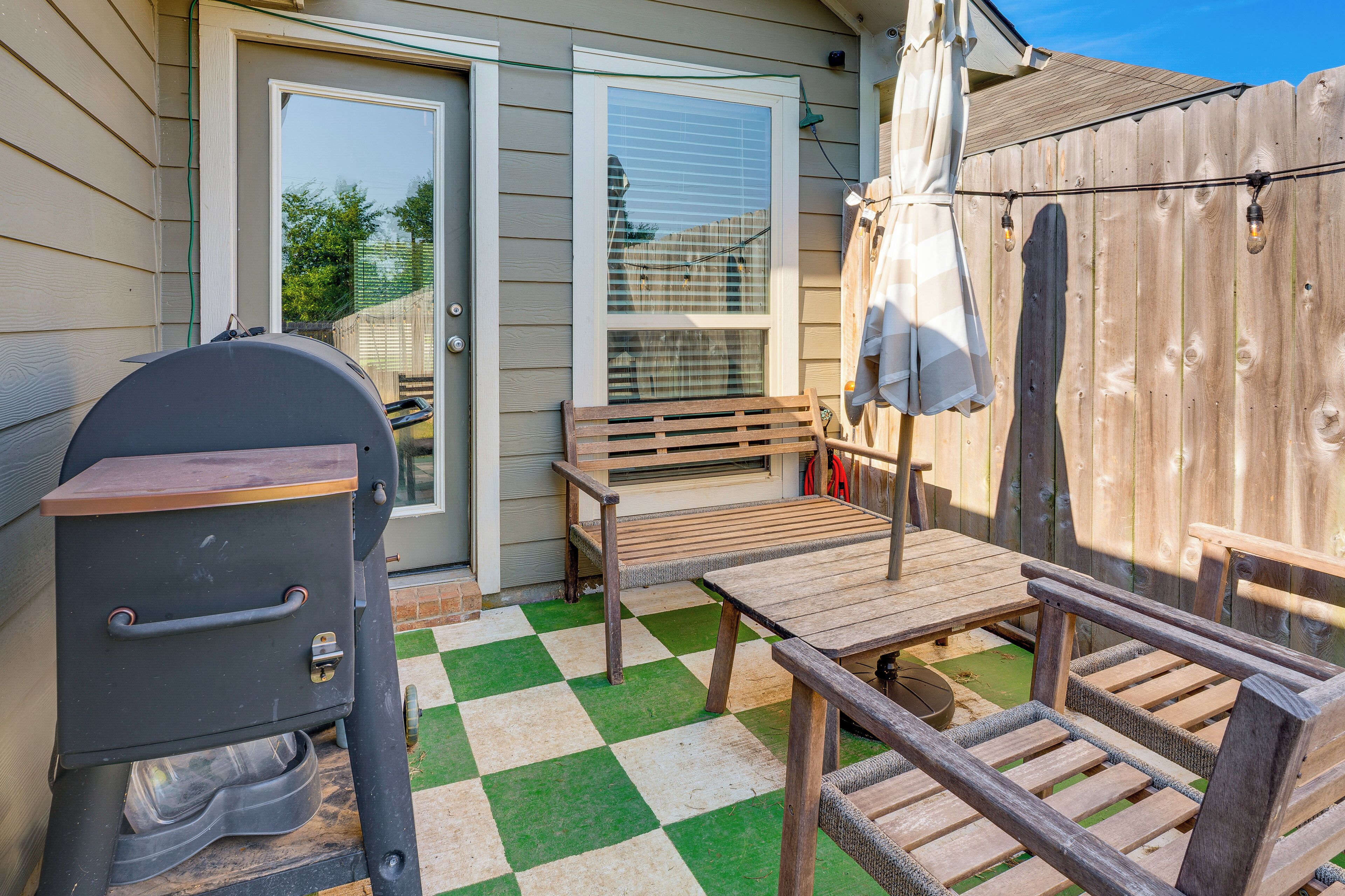 An outdoor patio with a grill, wooden table, and chairs.