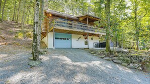 A two-story wooden cabin with a balcony, surrounded by trees and a gravel driveway. - < 1 Mi to Lake: Cabin w/ Hot Tub in Greentown! (Greentown)