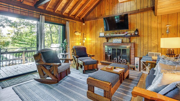 A wooden cabin interior with a fireplace, a television, and a deck area. - < 1 Mi to Lake: Cabin w/ Hot Tub in Greentown! (Greentown)