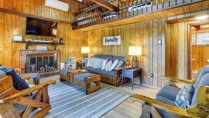 A cozy cabin interior with a fireplace, wooden furniture, and a sign that reads "family and friends gather here." - < 1 Mi to Lake: Cabin w/ Hot Tub in Greentown! (Greentown)