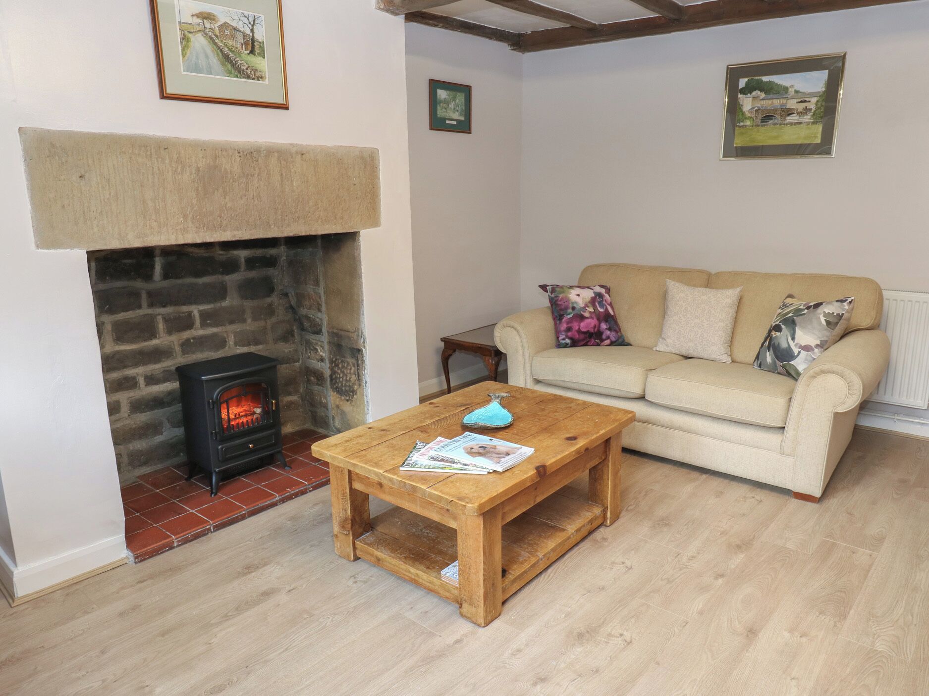 A cozy living room with a stone fireplace, a wooden coffee table, a beige sofa, and two framed pictures on the wall.