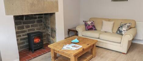 A cozy living room with a stone fireplace, a wooden coffee table, a beige sofa, and two framed pictures on the wall.