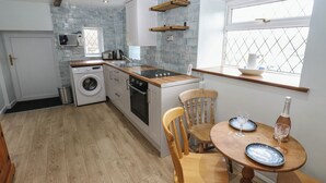 Une cuisine compacte équipée d’un lave-linge, d’un four et d’un plan de travail en bois. On y trouve une fenêtre avec vue, une table avec des chaises et un petit rebord de fenêtre sur lequel sont posés un bol et une bouteille.