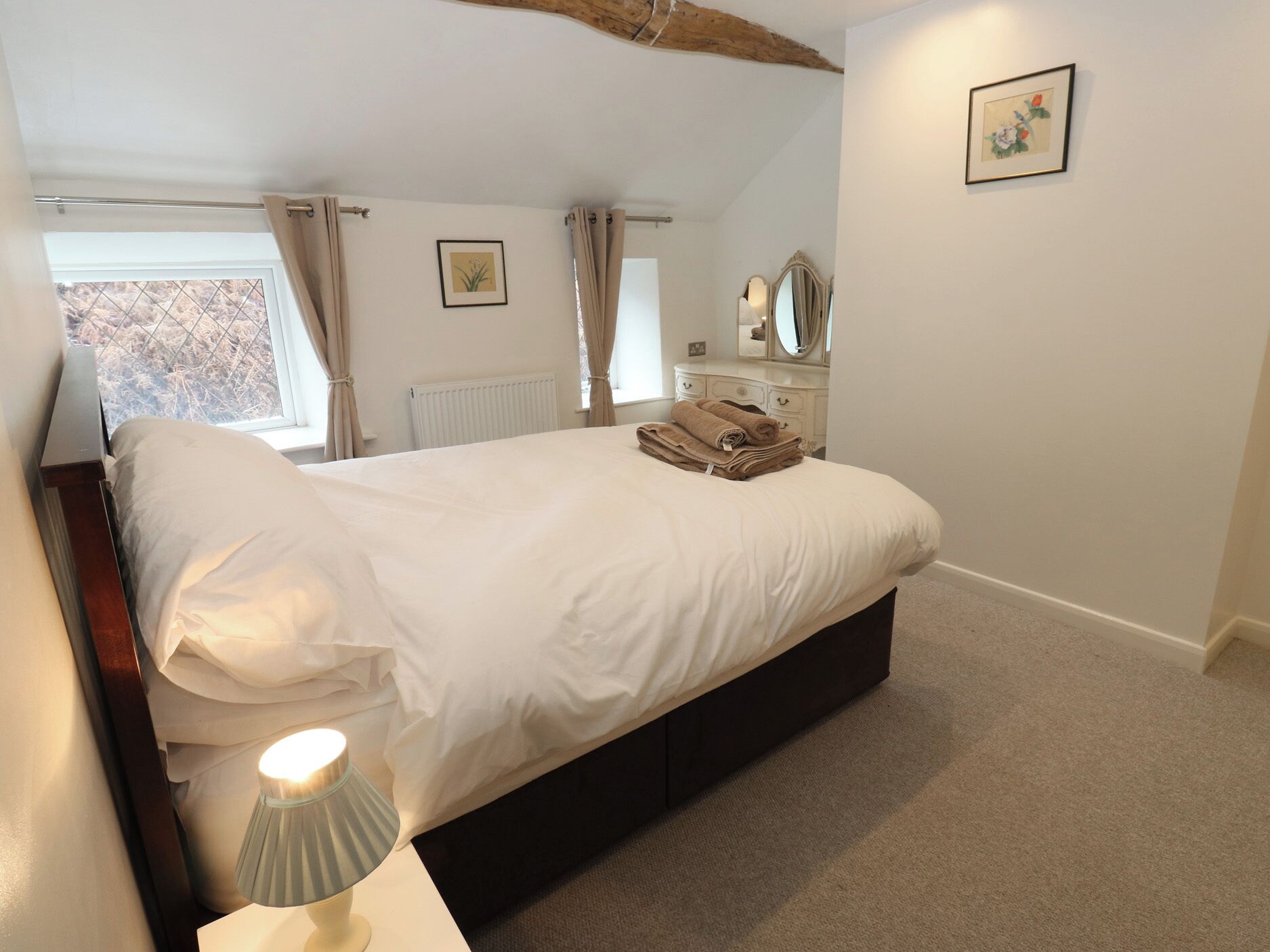 A bedroom with a bed, a bedside lamp, a dresser, a mirror, and a window with curtains.