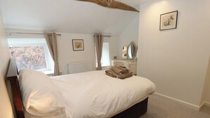 Une chambre à coucher avec un lit, une lampe de chevet, une commode, un miroir et une fenêtre avec des rideaux.