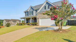 A two-story house with a garage, a front lawn, and a tree with pink flowers. - Fenced Yard & Patio! Family Home Near Fort Benning (Columbus)