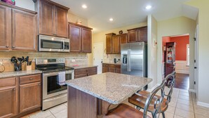 A kitchen with wooden cabinets, stainless steel appliances, a granite countertop, and a bar area with stools. - Fenced Yard & Patio! Family Home Near Fort Benning (Columbus)
