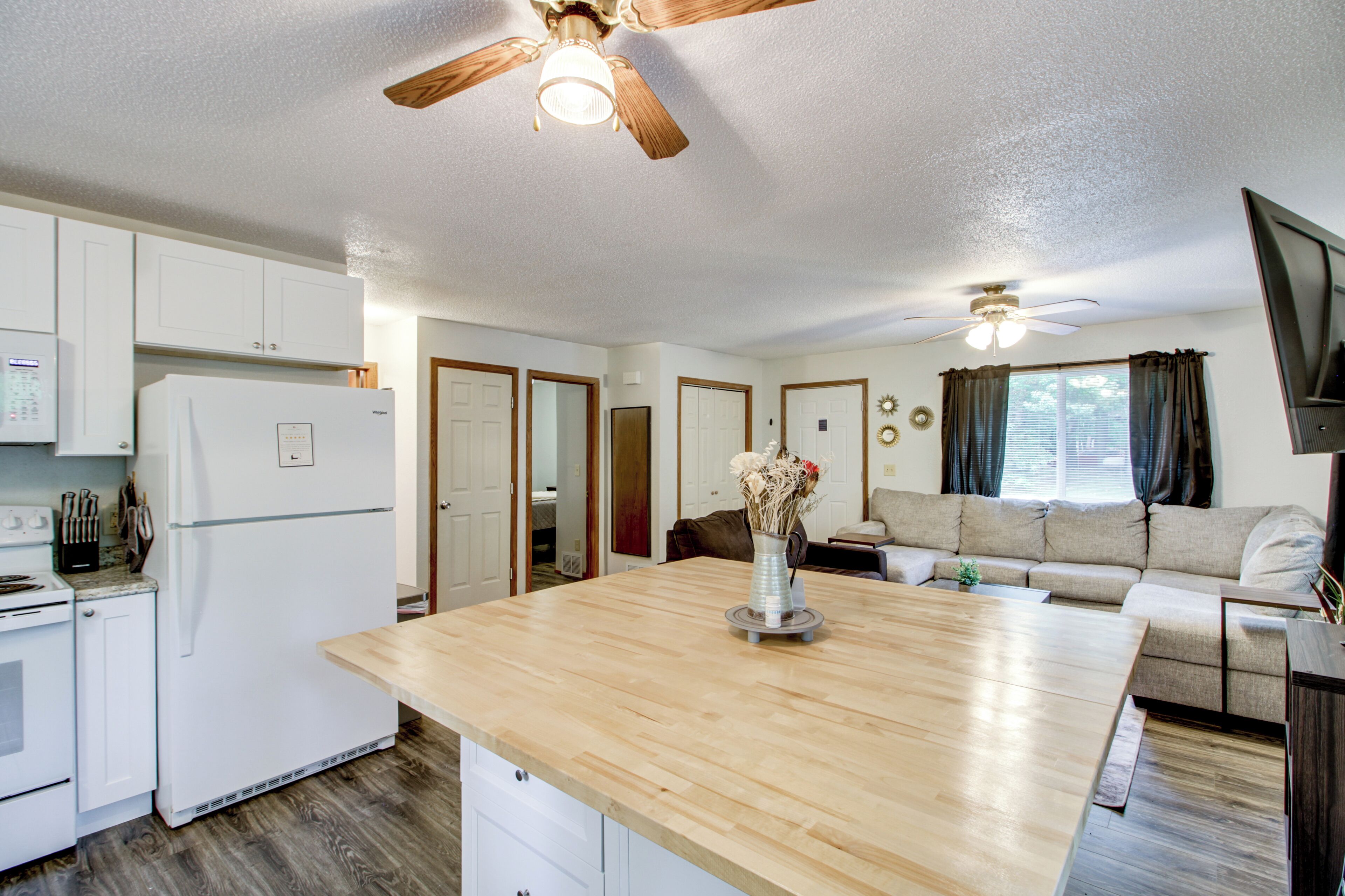 A modern kitchen with white cabinets, a wooden countertop, and a ceiling fan.