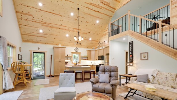 A spacious living area with a high ceiling, wooden flooring, a central seating area with a round coffee table, a sofa, and a staircase leading to an upper level. - Paddle, Play & Relax: Home w/ Pioneer Lake Access! (Conover)