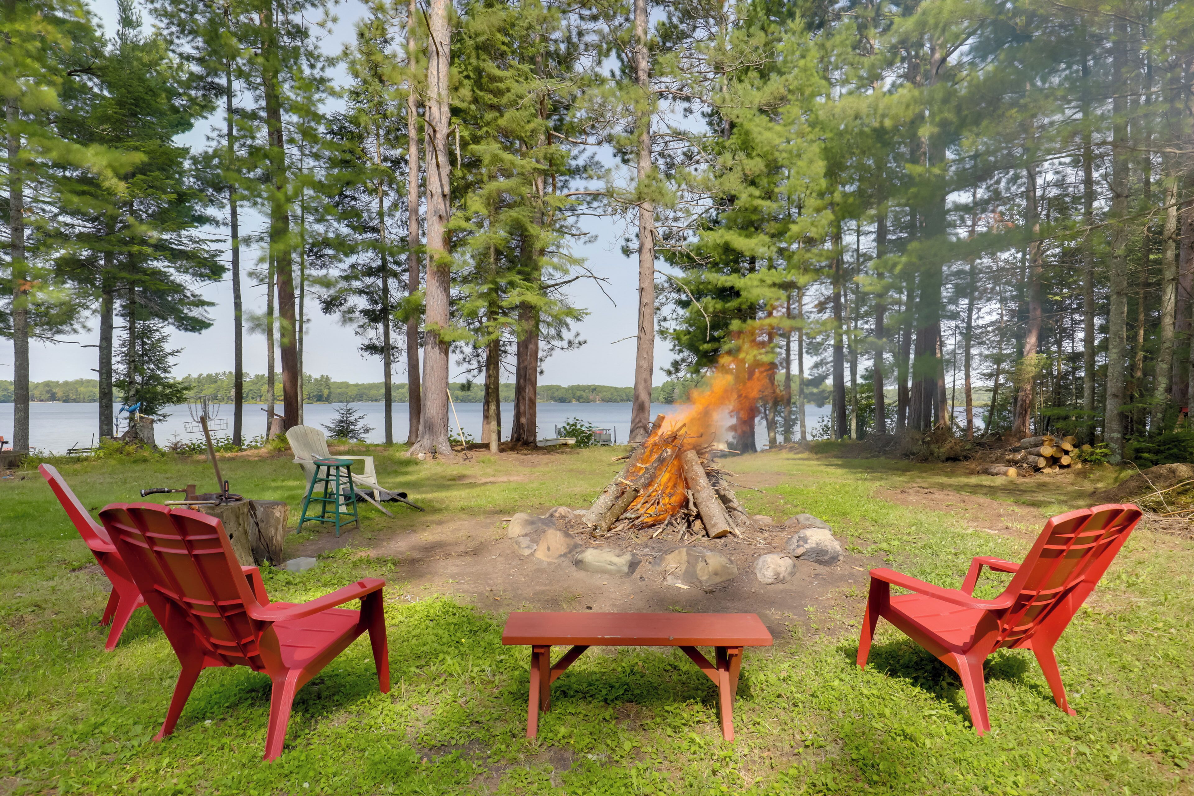 A campsite with two red chairs, a picnic table, and a campfire.
