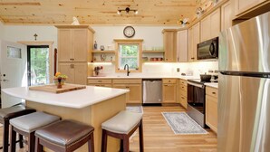 A modern kitchen with wooden cabinets, stainless steel appliances, and a central island with stools. - Paddle, Play & Relax: Home w/ Pioneer Lake Access! (Conover)