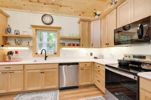 Une cuisine moderne avec des meubles en bois, des appareils en acier inoxydable et une fenêtre donnant sur un paysage verdoyant.